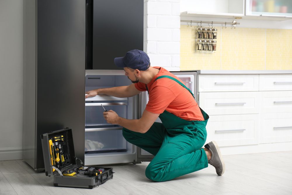 Man in Overalls Repairs a Refrigerator in a Kitchen, With Tools Visible — Industry Fire Services in Weipa, QLD