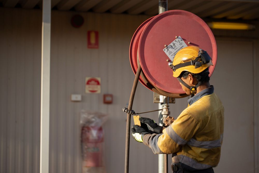 Worker in Yellow Uniform and Hard Hat Inspecting a Red Fire Hose — Industry Fire Services in Cape York, QLD