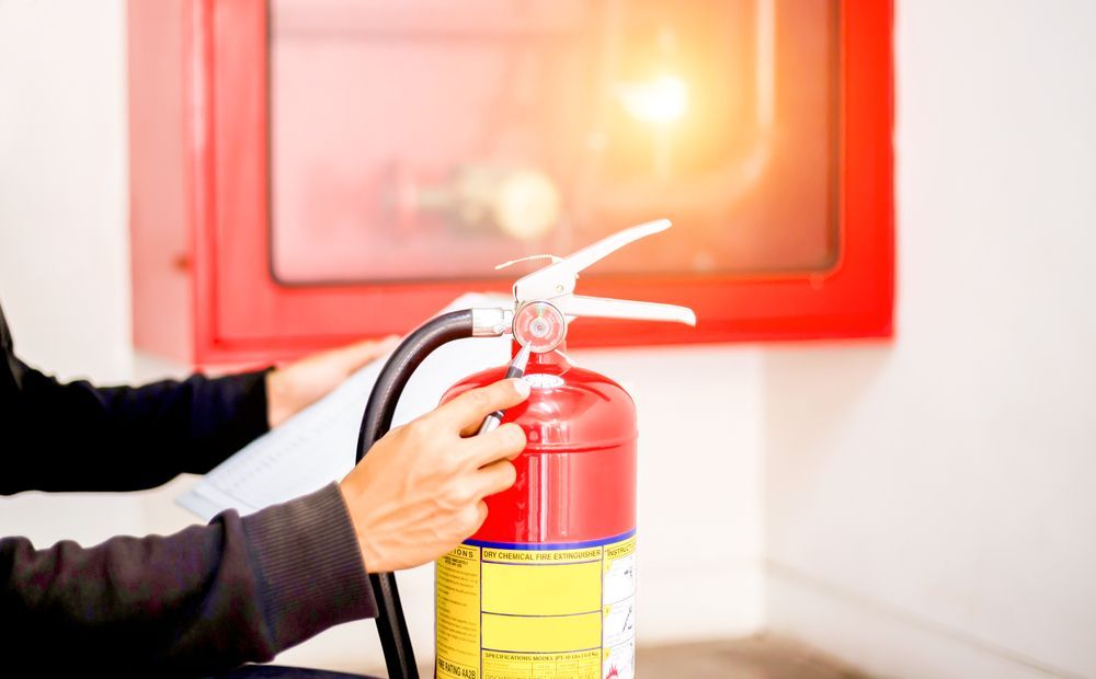 Person Holding a Red Fire Extinguisher Near a Wall-mounted Red Fire Hose Cabinet — Industry Fire Services in Proserpine, QLD
