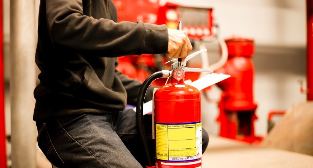 Person Checking a Red Fire Extinguisher in a Utility Room — Industry Fire Services in Proserpine, QLD