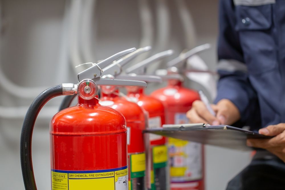 Person Inspecting Fire Extinguishers, Writing on a Clipboard in a Storage Area — Industry Fire Services in Weipa, QLD