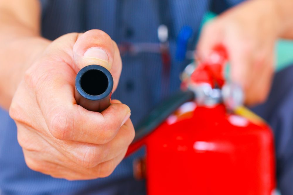 Person Holding the Nozzle of a Red Fire Extinguisher, Pointing It Forward — Industry Fire Services in Weipa, QLD
