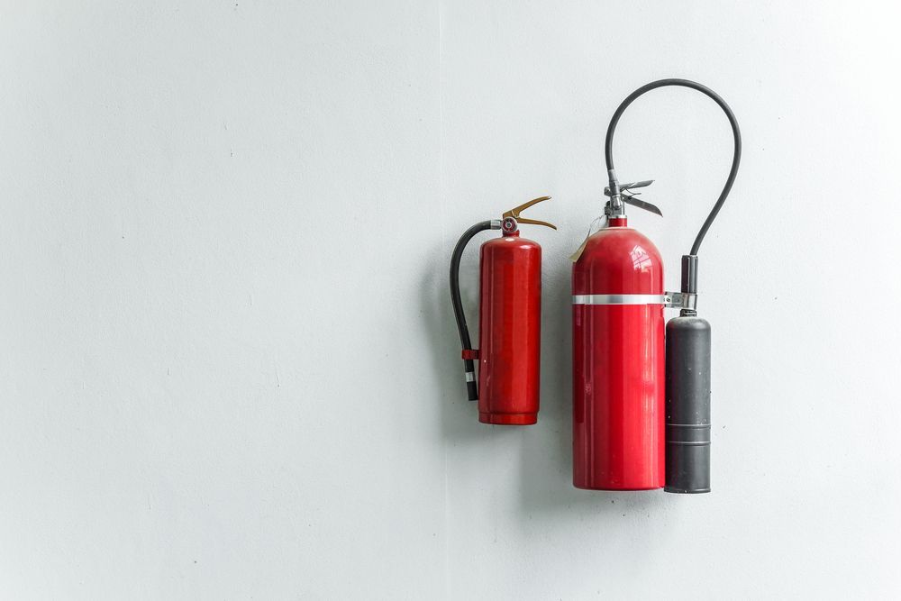 Two Red Fire Extinguishers Hanging on a White Wall — Industry Fire Services in Toowoomba, QLD