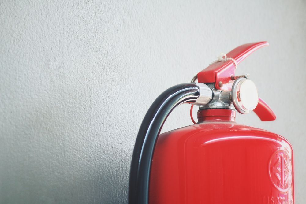 Red Fire Extinguisher Against a Gray Wall — Industry Fire Services in Port Douglas, QLD