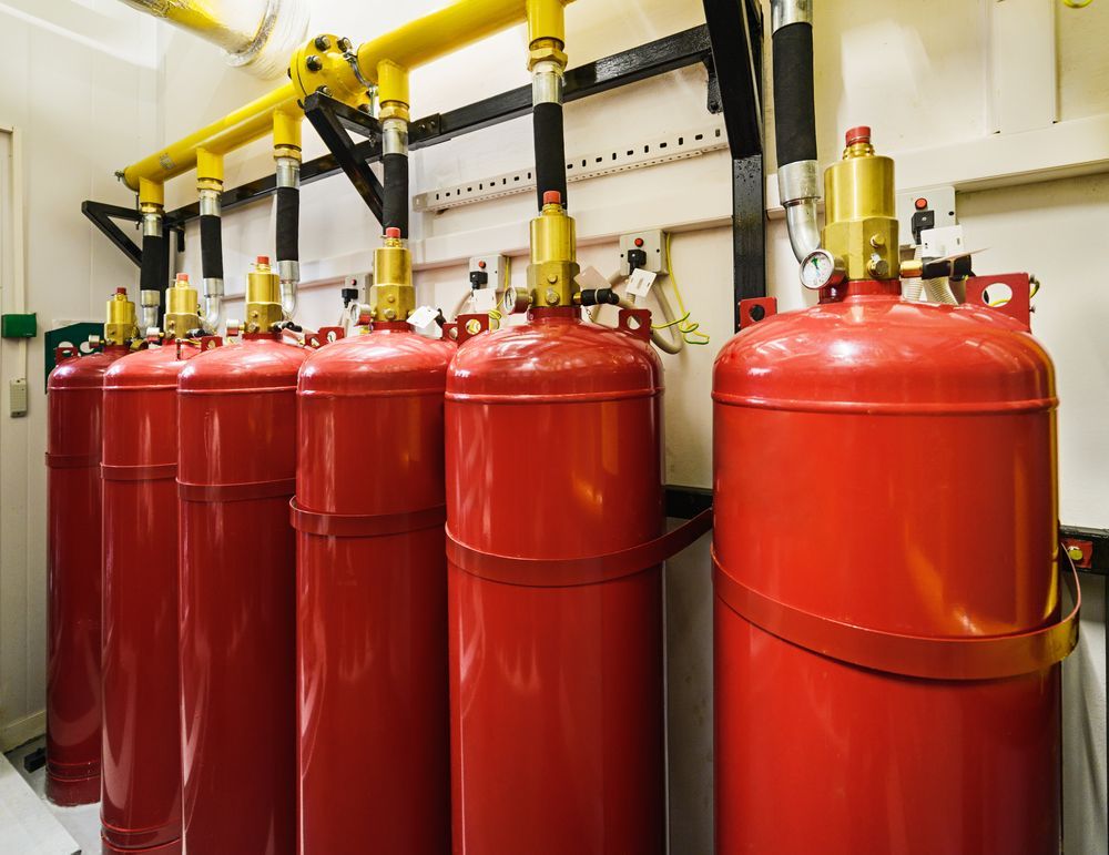 Row of Red Fire Suppression Cylinders in a Room With Yellow Pipes — Industry Fire Services in Port Douglas, QLD