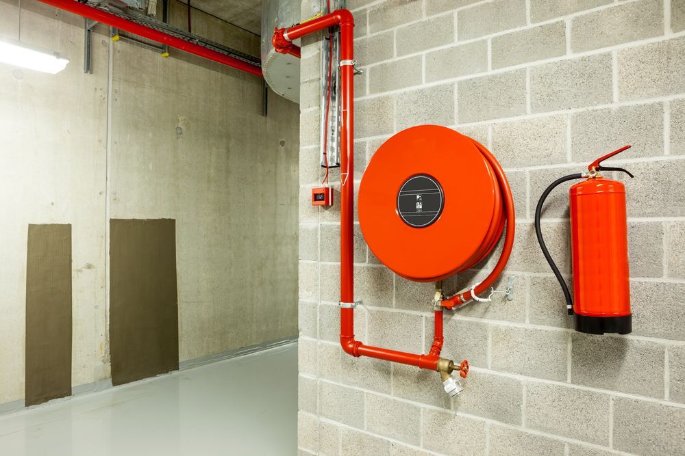 Red Fire Hose Reel and Fire Extinguisher on a Gray Brick Wall in a Building — Industry Fire Services in Bowen, QLD