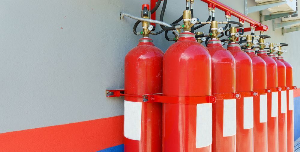 Red Fire Suppression Gas Cylinders, Mounted in a Row on a Gray Wall — Industry Fire Services in Atherton Tablelands, QLD
