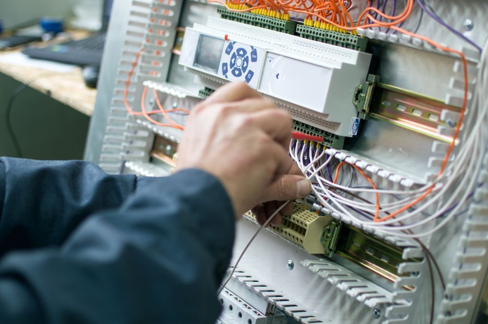 Person Wiring Electrical Components Inside a Metal Cabinet — Industry Fire Services in Ingham, QLD