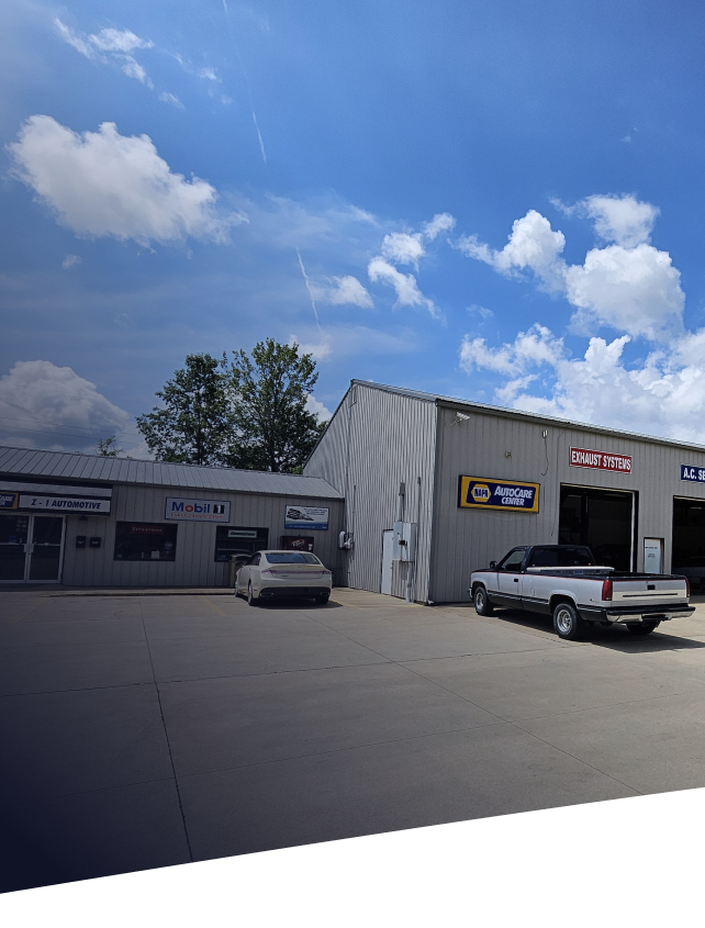 A car repair shop with two buildings, vehicles, and a partly cloudy blue sky overhead. | Z-1 Automotive, Inc.