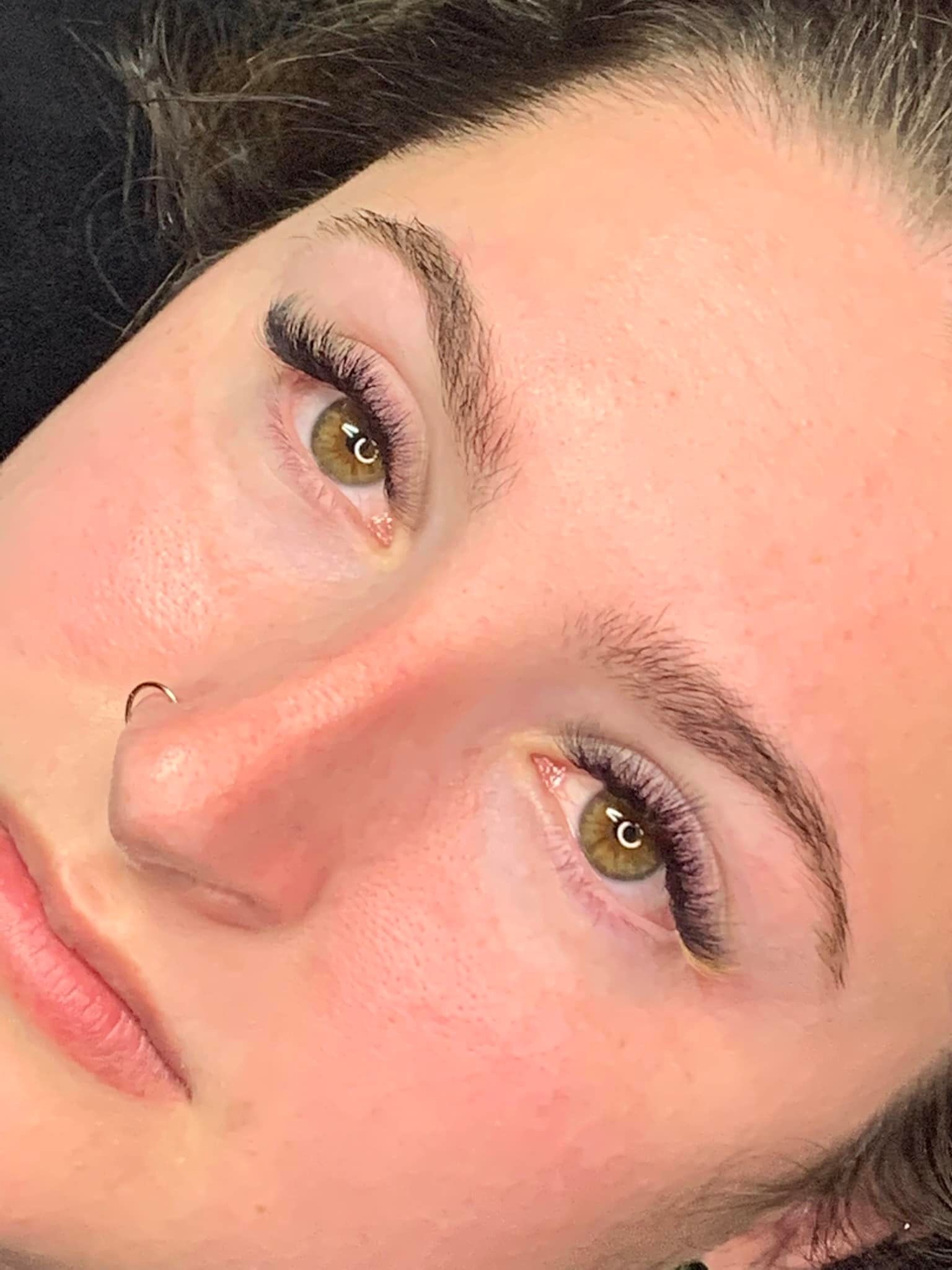 A close up of a woman 's face with long eyelashes and a nose ring.