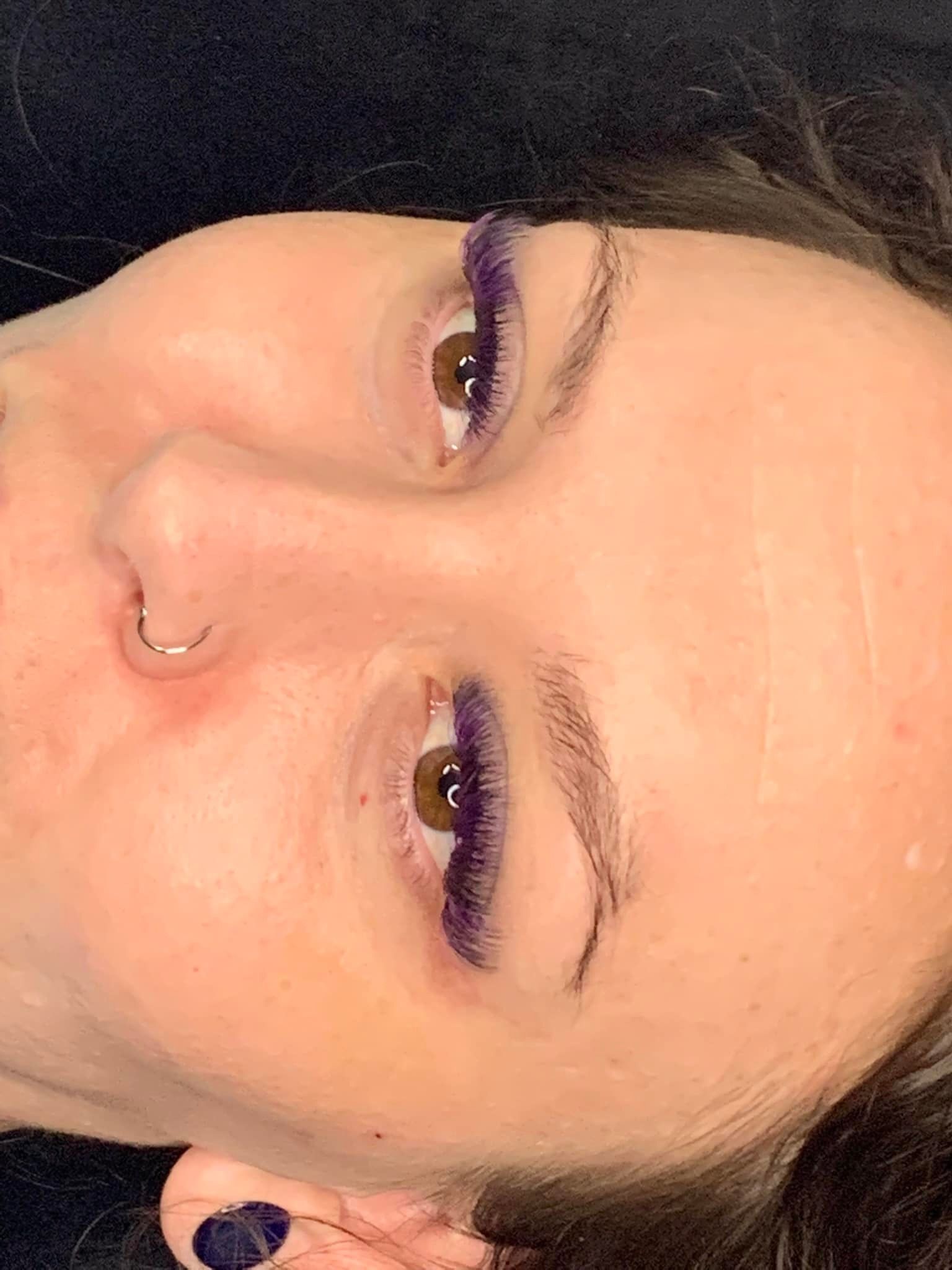 A close up of a woman 's face with purple eyelashes and a nose ring.