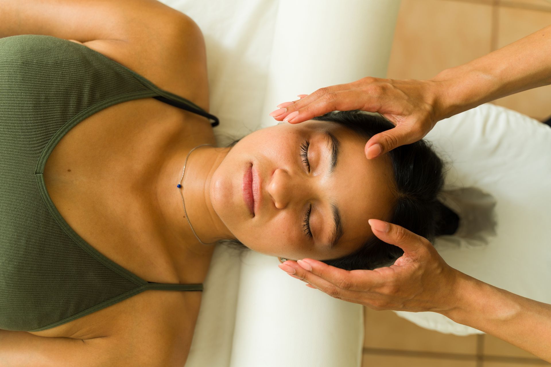 A woman is laying on a bed getting a head massage.