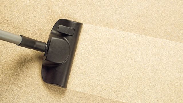 A vacuum cleaner head moving over a beige carpet, creating a clean, dust-free stripe.