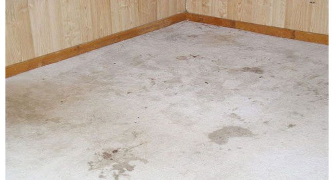 A light gray concrete floor with visible dark stains, meeting a wooden baseboard along a light-colored wooden wall.