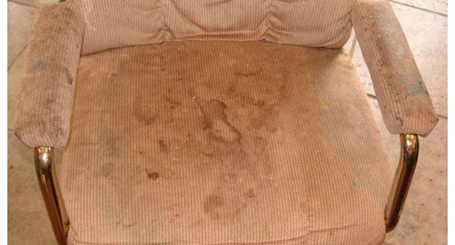 A worn, beige upholstered armchair with a gold metal frame, showing significant staining and fabric wear.