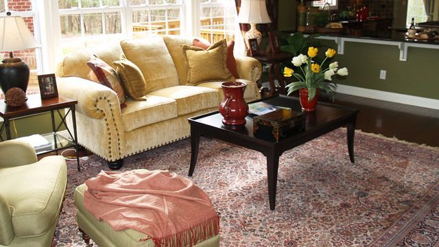 A light yellow sofa, ottoman with a pink throw, and a dark coffee table with yellow flowers, set on an ornate rug.