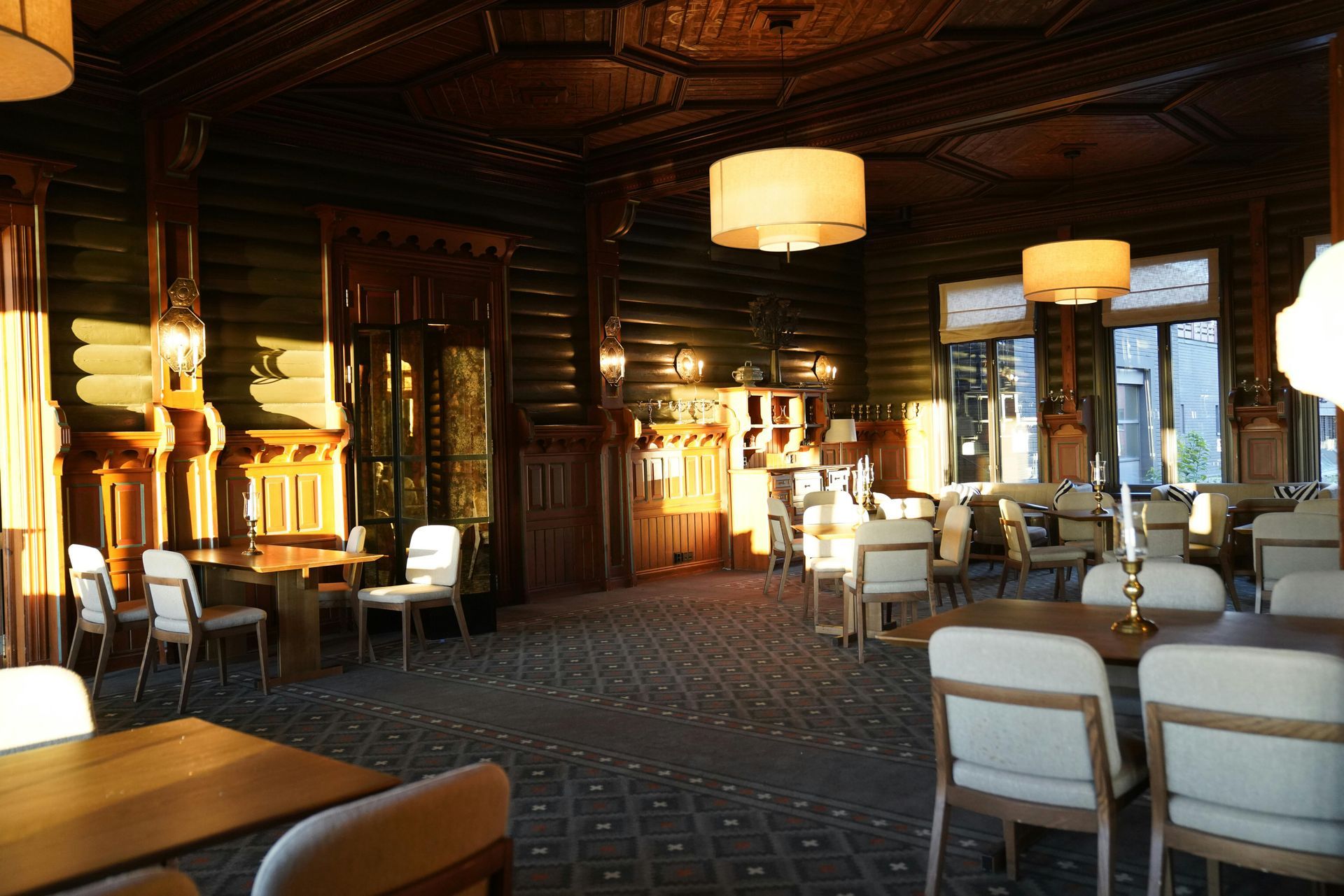 An interior view of a rustic, log-cabin style restaurant with dark wood walls, pendant lighting, and arranged tables.