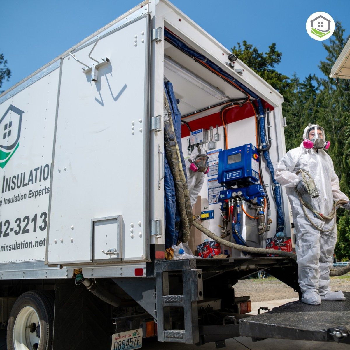 White truck with open door, insulation technician in protective suit and respirator, spraying.