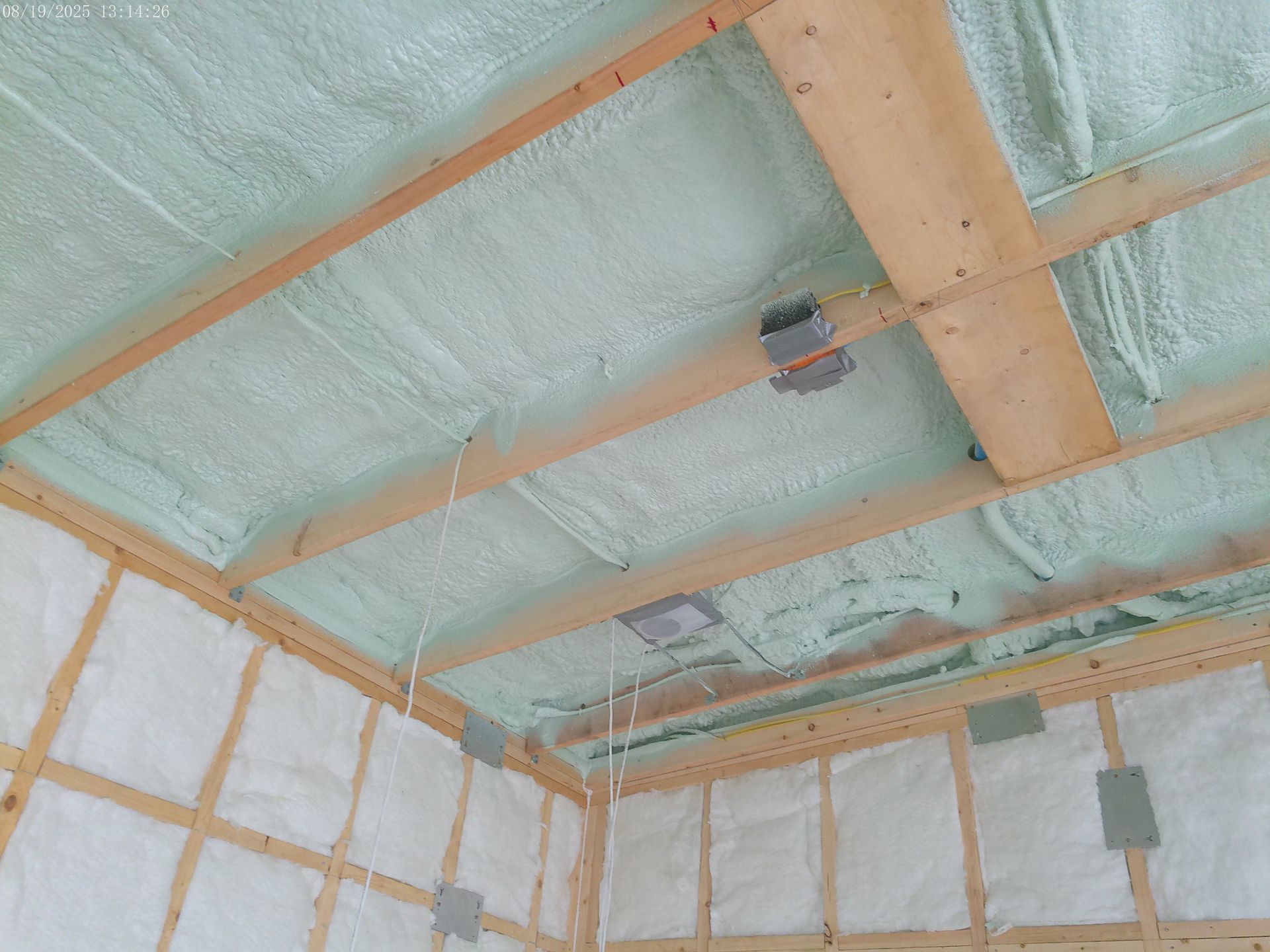 A room under construction with green spray foam insulation on the ceiling and white batt insulation on the walls.