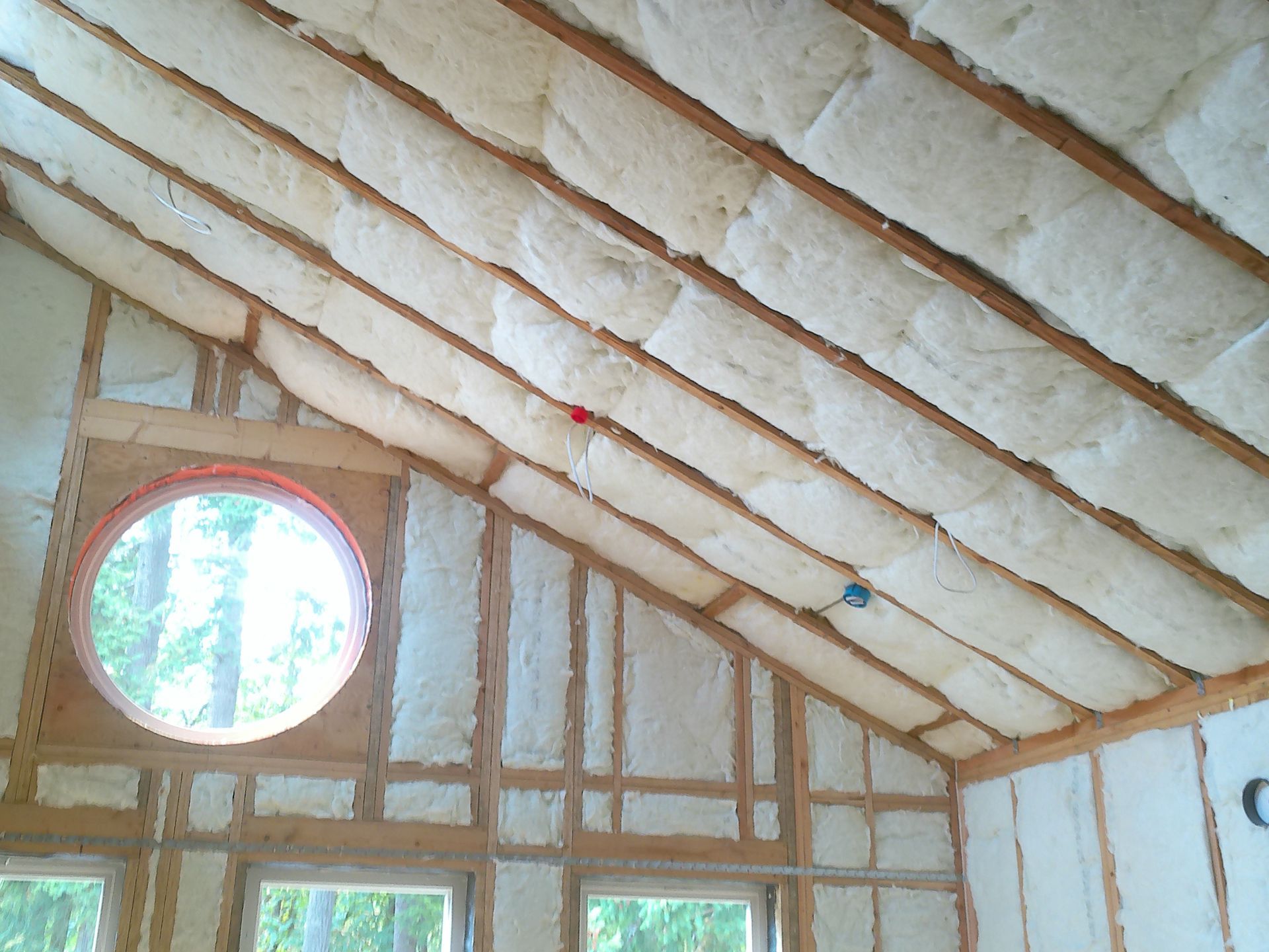 Interior view of a slanted ceiling with installed white fiberglass insulation batts between exposed wooden rafters.