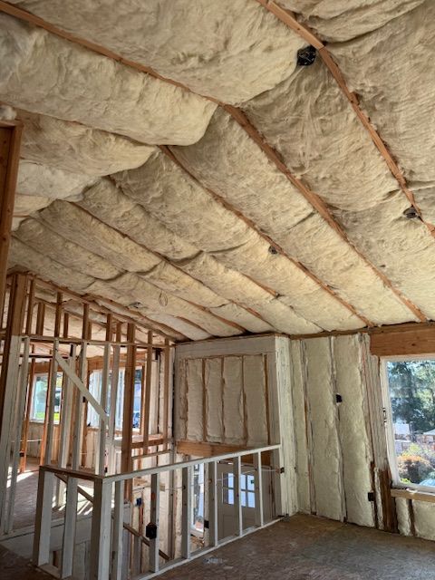 An unfinished room with vaulted ceilings and walls insulated with thick, beige fiberglass batts between wooden studs.
