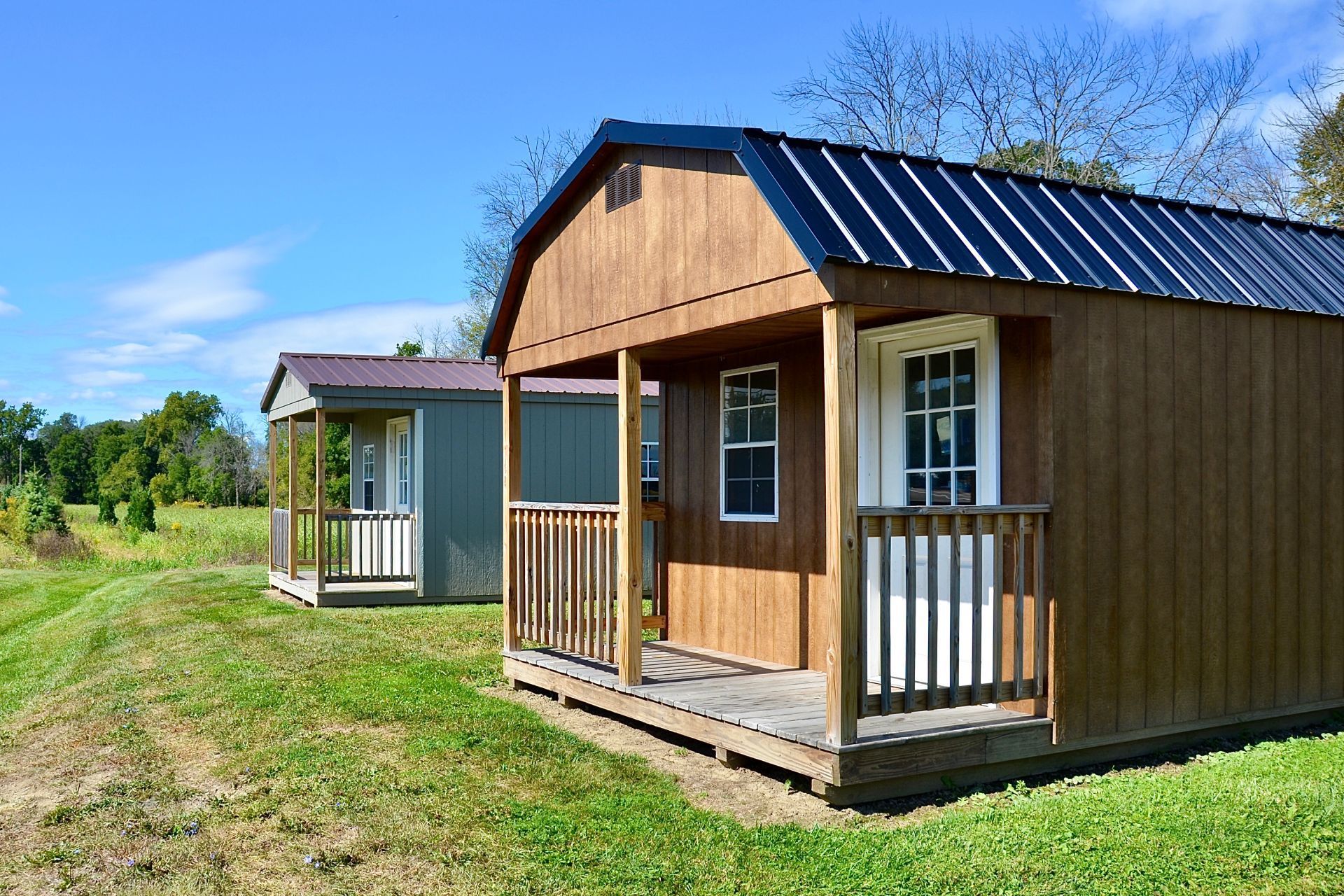 Two small sheds with porches are sitting next to each other in a grassy field.