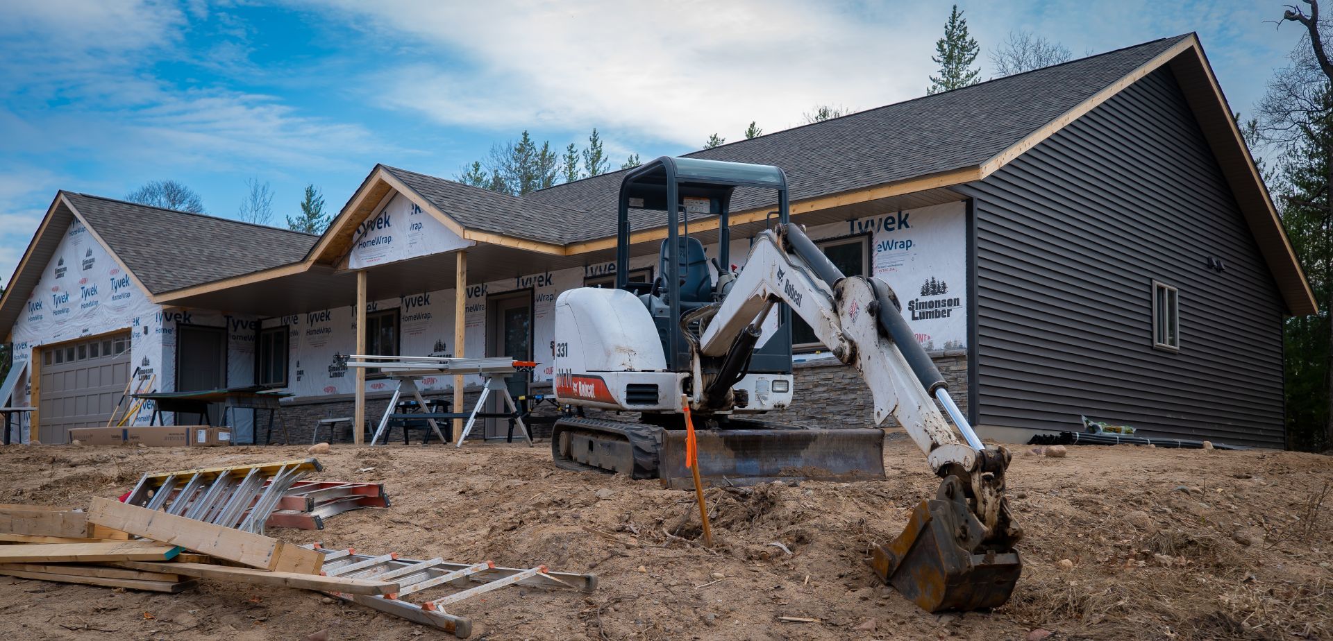 A small excavator is parked in front of a house under construction.