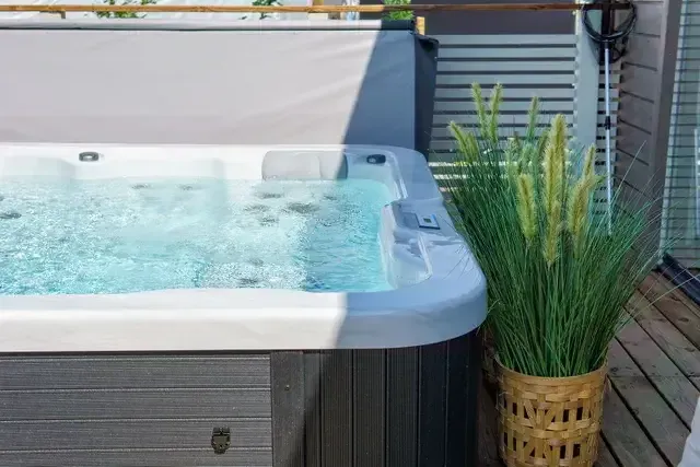 Outdoor hot tub with clear water on a patio, surrounded by greenery and flowers.