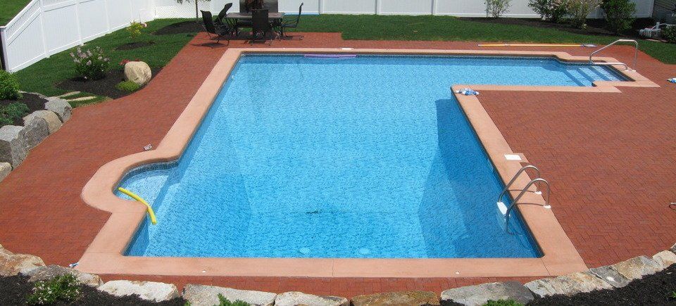 Backyard swimming pool with blue water, red patio decking, and a diving board