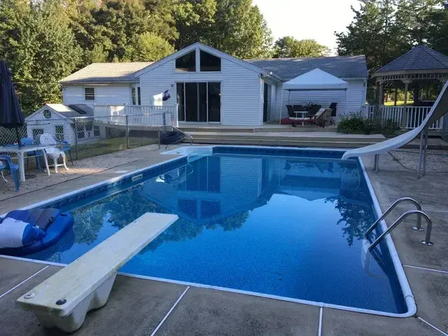 Backyard swimming pool with diving board, house, and trees at dusk