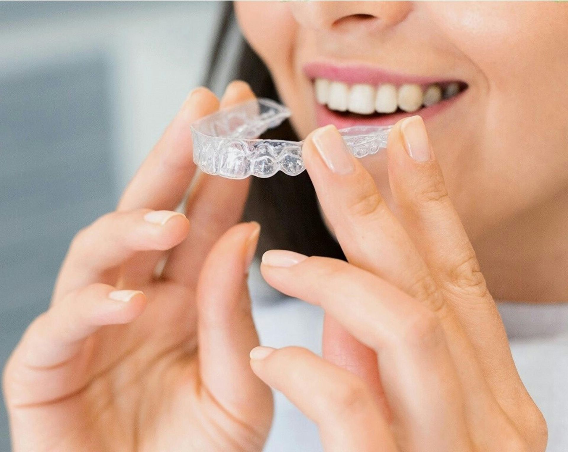 Woman inserting clear aligner into her mouth; smiling, close-up shot.