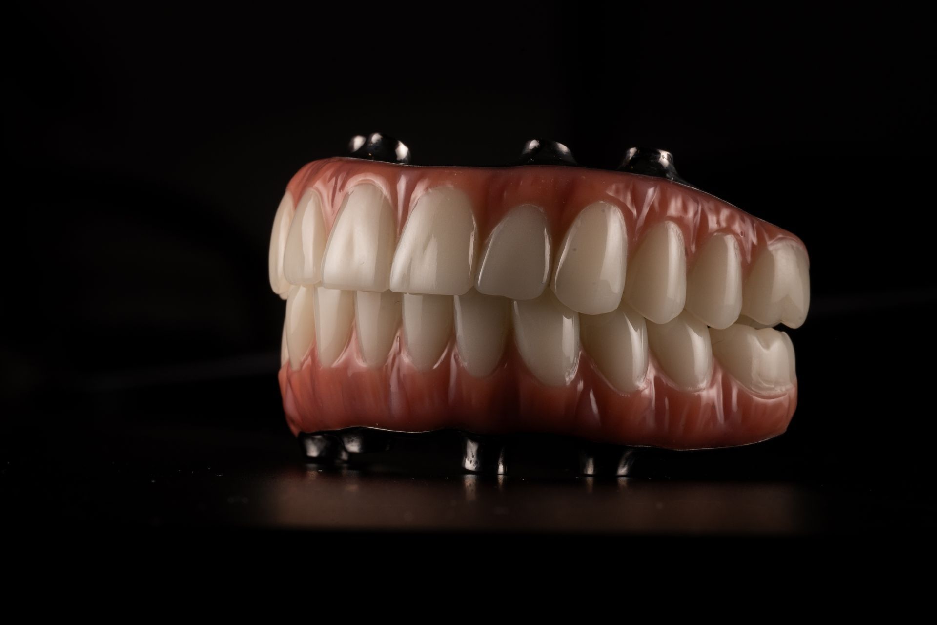 Dentures on posts; pink gums, white teeth. Black background.