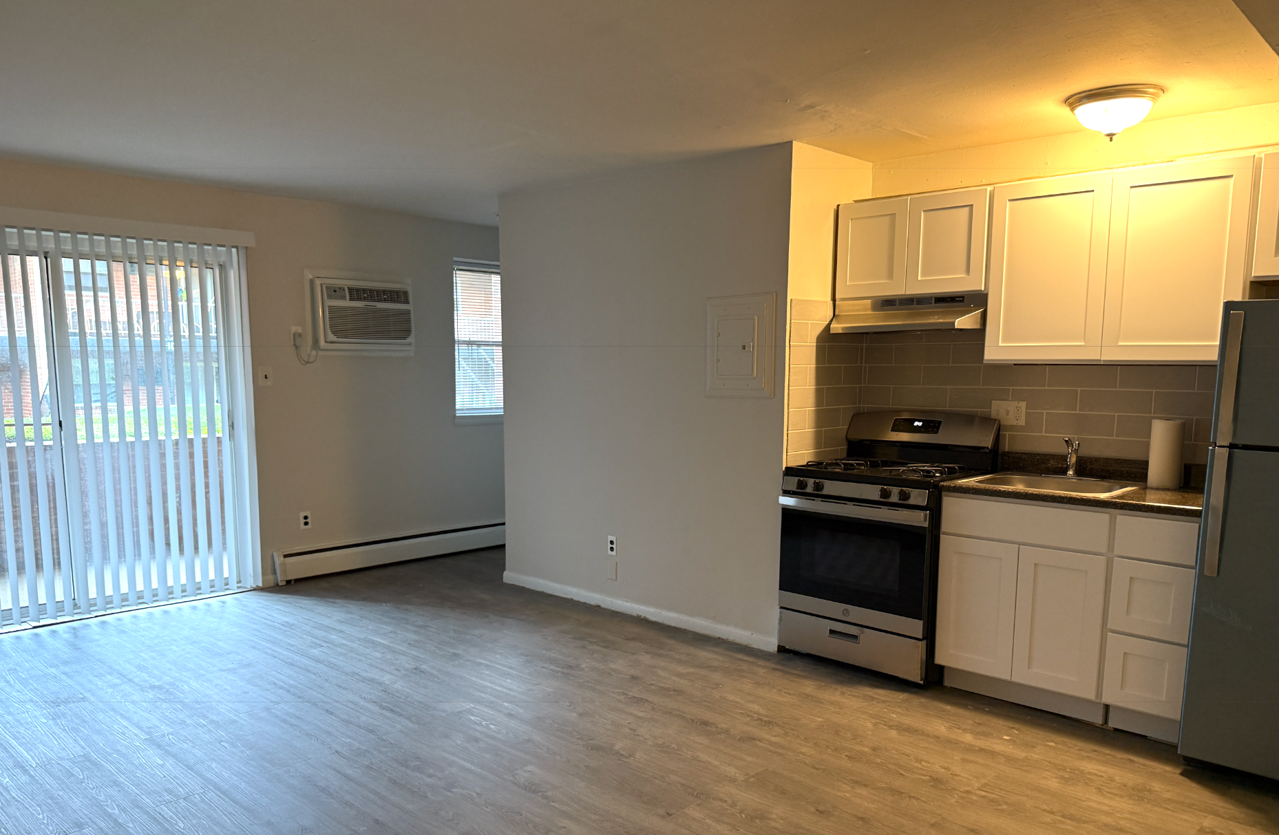 A small apartment with light-colored flooring, a kitchen featuring white cabinets, stainless appliances, and a balcony.