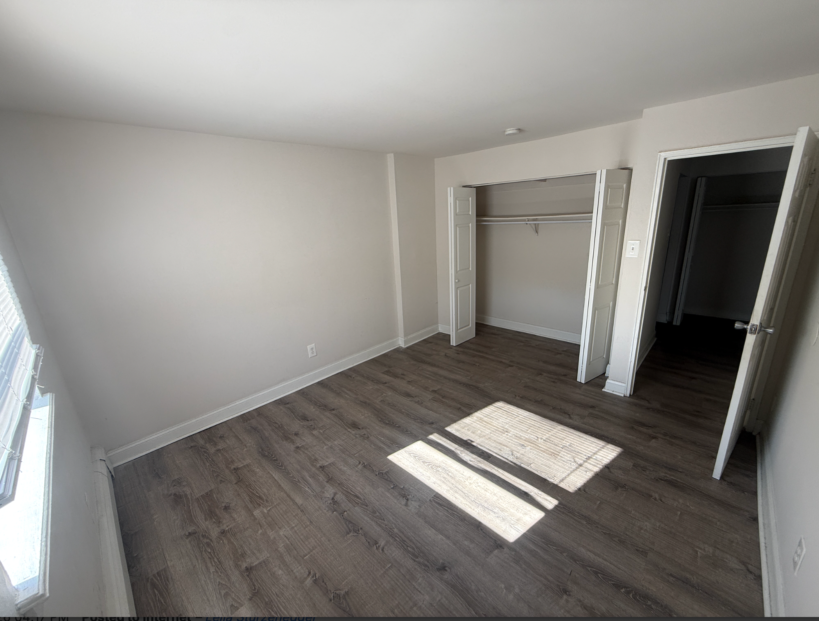 An empty bedroom with light-colored walls, wood-look flooring, a closet with open bifold doors, and an open doorway.