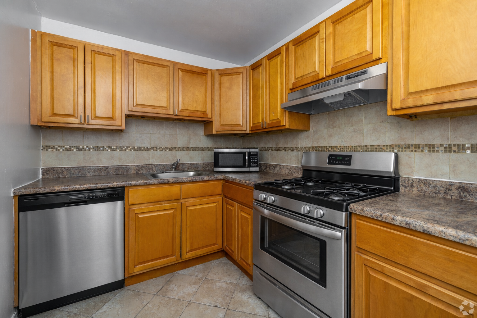 A kitchen with wooden cabinets, stainless steel appliances, a tiled backsplash, and stone-look countertops.