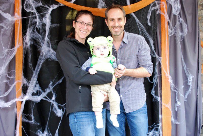 A man and woman are holding a baby in a frog costume.