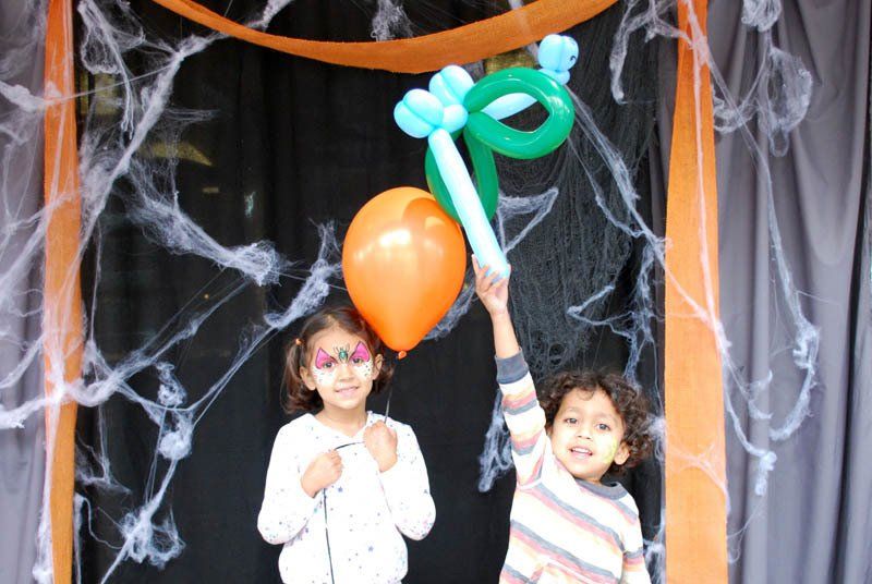 A boy and a girl are holding balloons in front of a spider web.