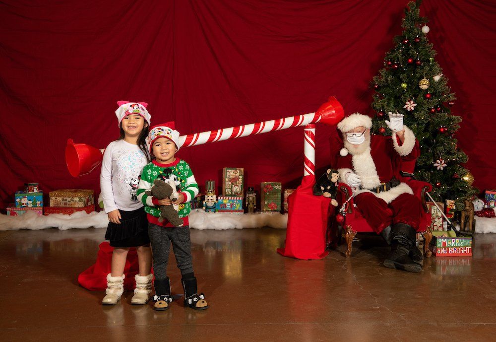 Two children are posing for a picture with santa claus in front of a christmas tree.