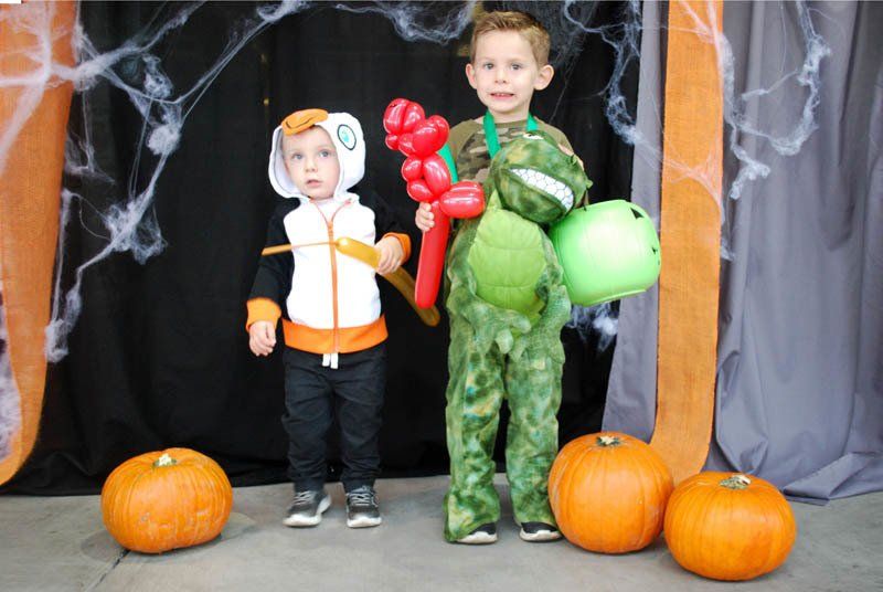 Two young boys in halloween costumes standing next to pumpkins