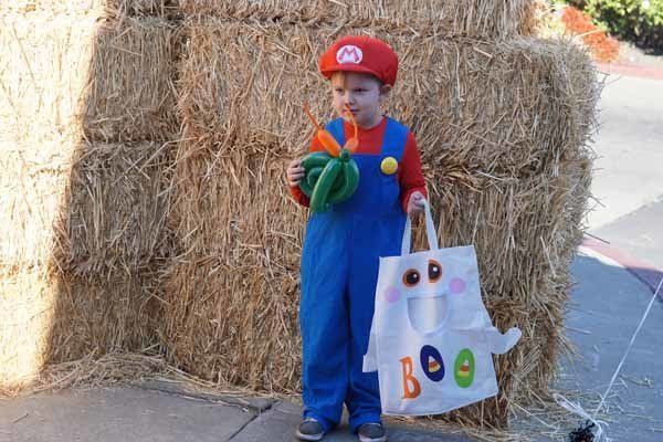 A little boy in a mario costume is holding a pumpkin and a boo bag
