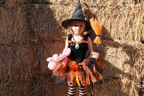 A little girl dressed as a witch is holding balloons and a broom.