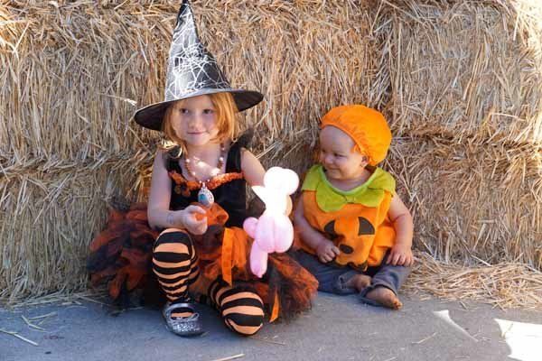A little girl in a witch costume sits next to a baby in a pumpkin costume