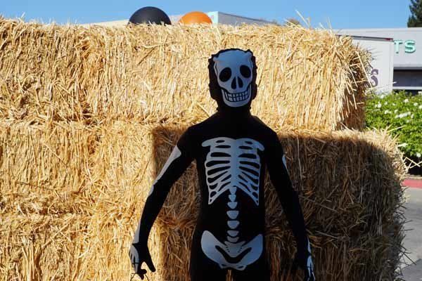 A person in a skeleton costume is standing in front of hay bales