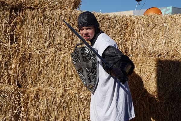 A person in a costume is standing in front of hay bales.