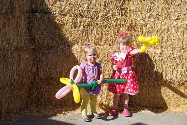 Two little girls are holding balloons in front of a hay bale.