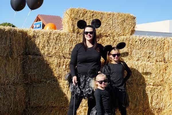 A woman and two children in mickey mouse costumes are standing in front of hay bales.