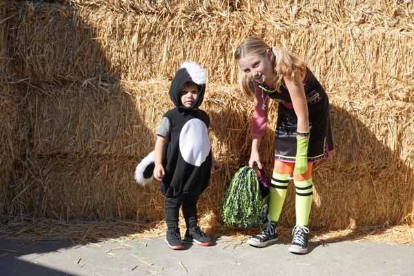 A boy and a girl in costumes are standing next to each other in front of a hay bale.