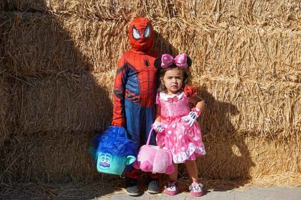 A boy in a spiderman costume and a girl in a minnie mouse dress are standing next to each other.