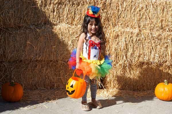 A little girl in a clown costume is holding a trick or treat bucket.