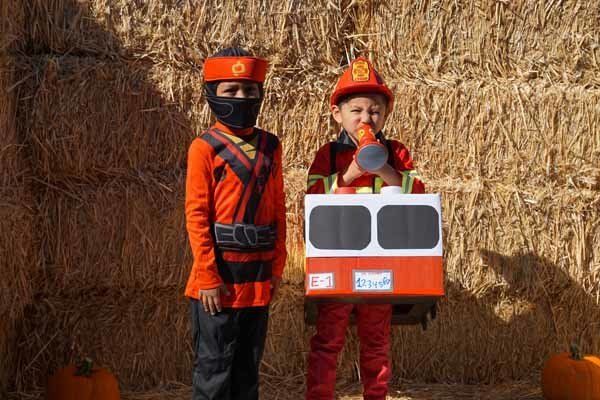Two children in costumes are standing next to each other in front of a hay bale.